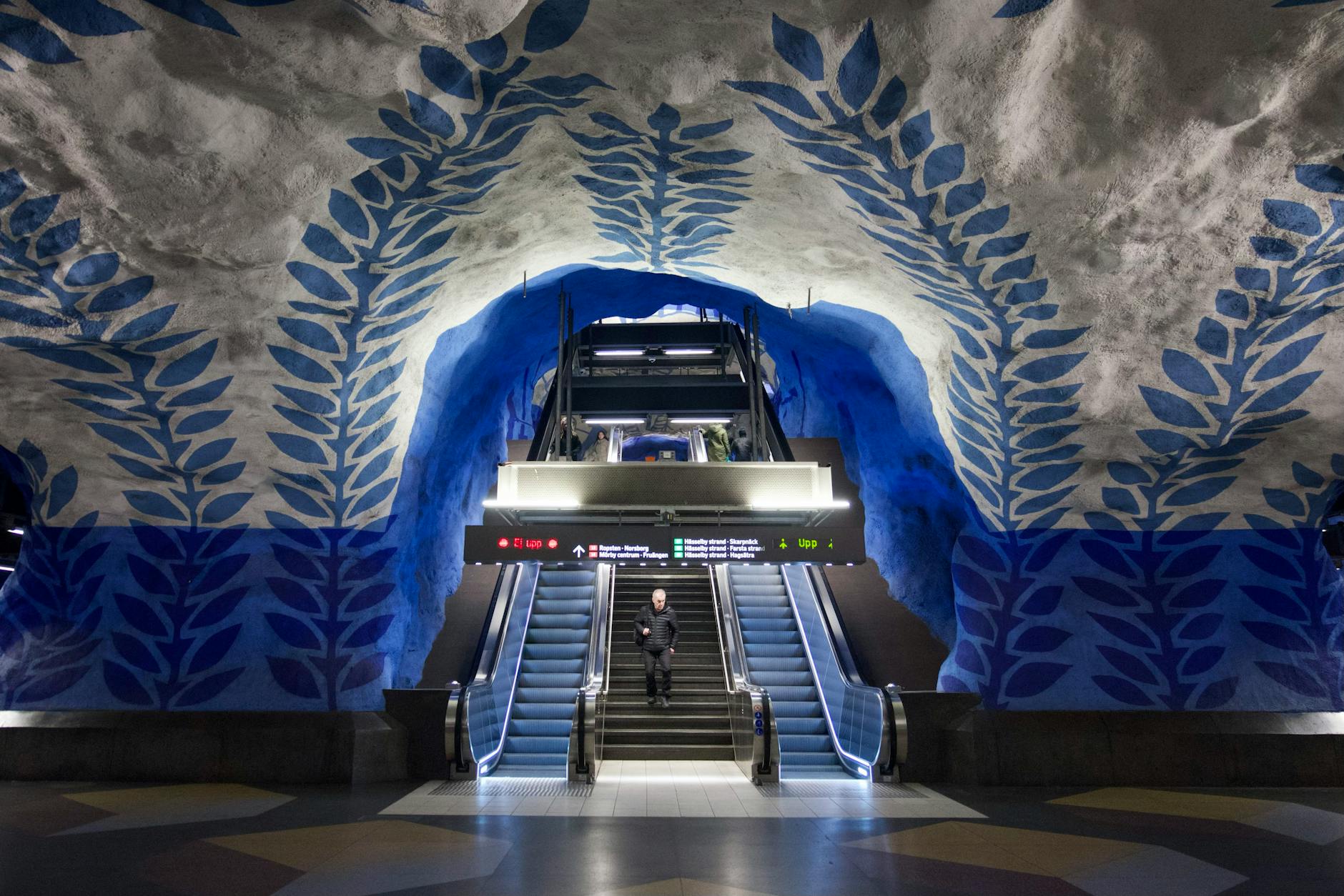 Vivid painted blue leaf patterns on the rock walls of a Stockholm Tunnelbana metro station