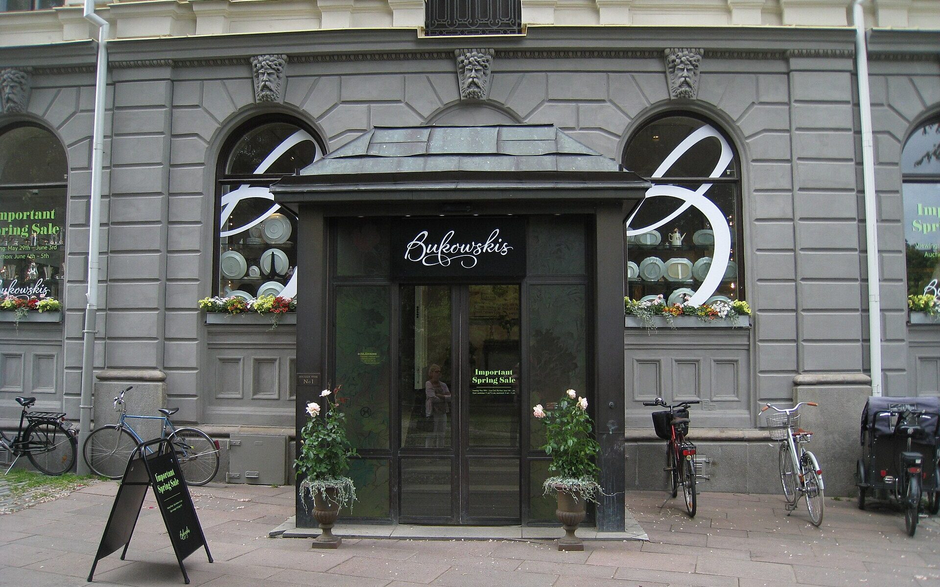 The dark wooden entrance porch of the Bukowskis auction house at Berzelii Park in Stockholm, with bicycles parked outside