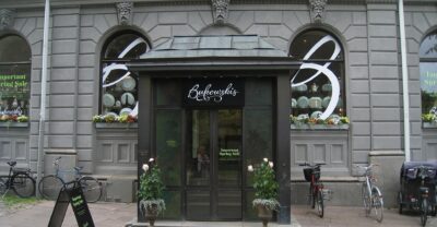 The dark wooden entrance porch of the Bukowskis auction house at Berzelii Park in Stockholm, with bicycles parked outside