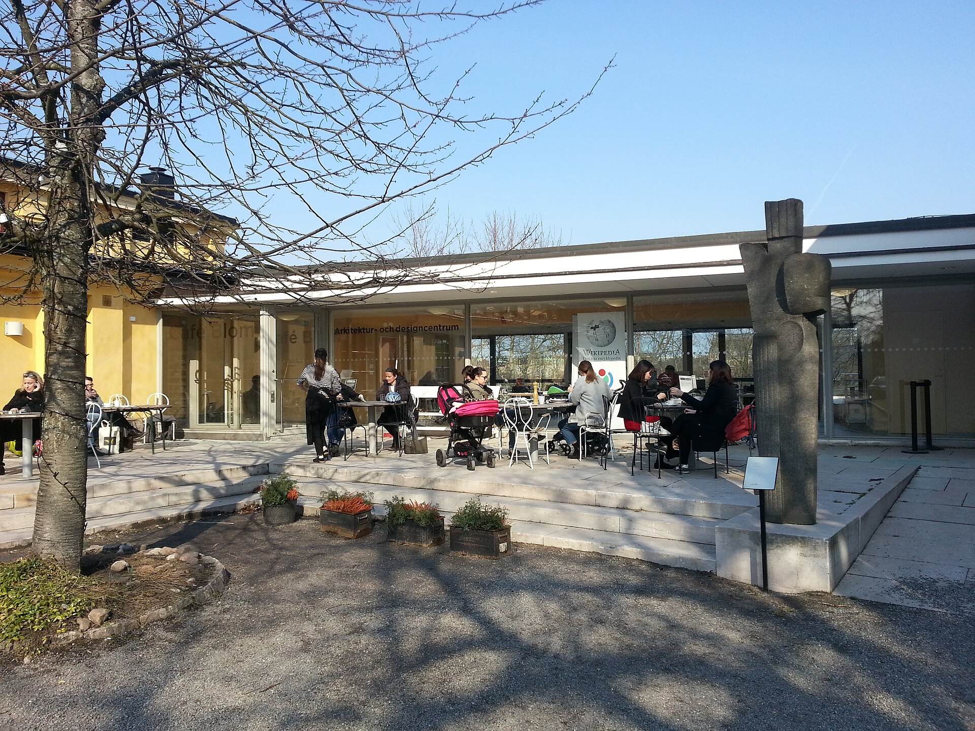 People sitting at tables on the sunny outdoor terrace of the ArkDes café on Skeppsholmen