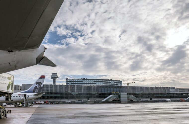 Norwegian aircraft parked at the gates of Arlanda airport, with the control tower and the long glass terminal behind under a cloudy sky