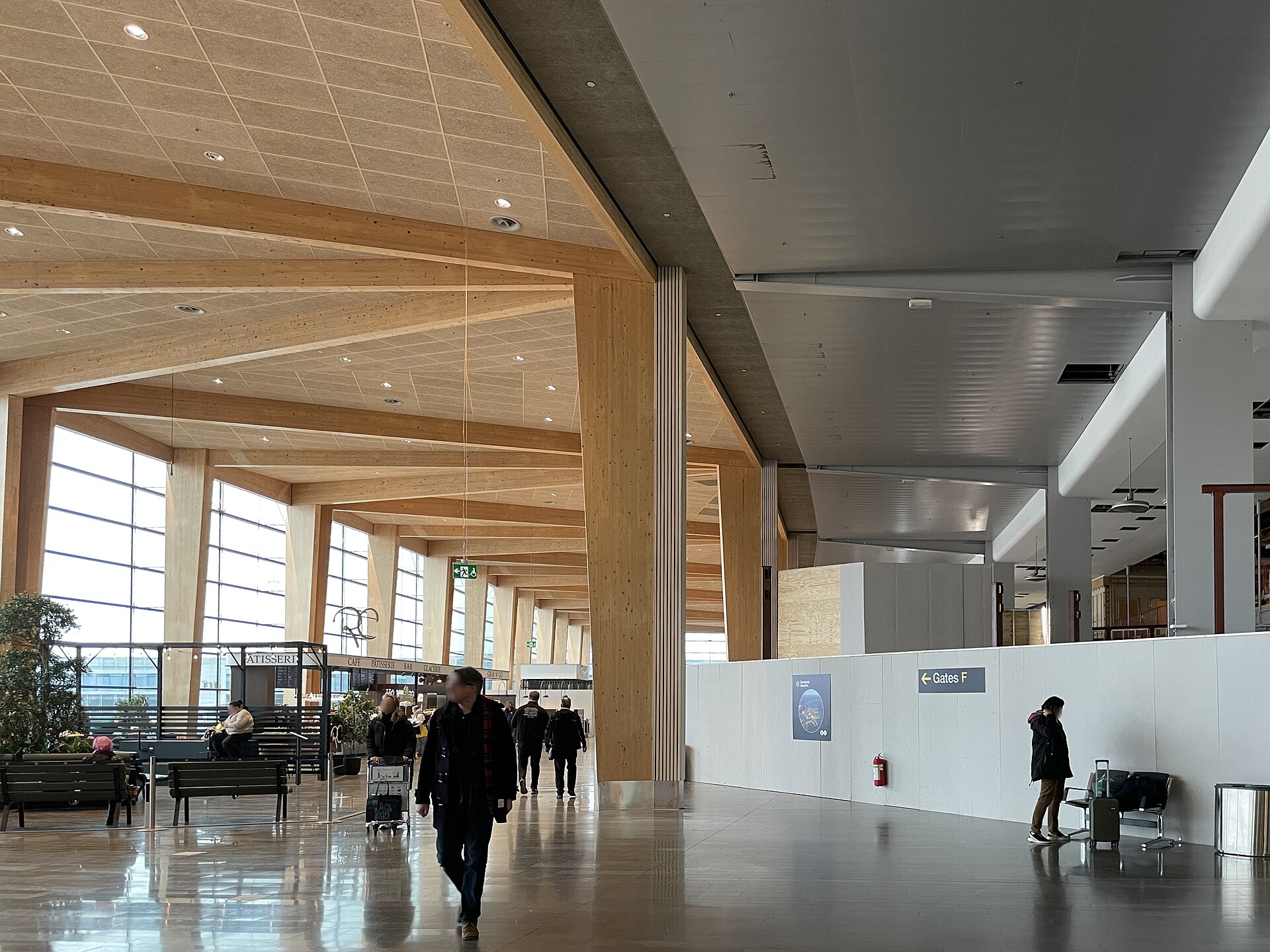 A bright timber-roofed concourse in Arlanda Terminal 5 with large windows, benches and a sign pointing to the F gates