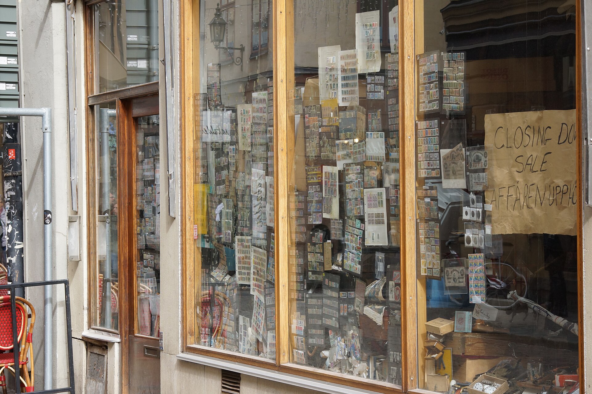 The window of a small antiques and curios shop on Stora Nygatan in Gamla Stan, packed with stamps and small objects, with a hand-written closing-down sale sign