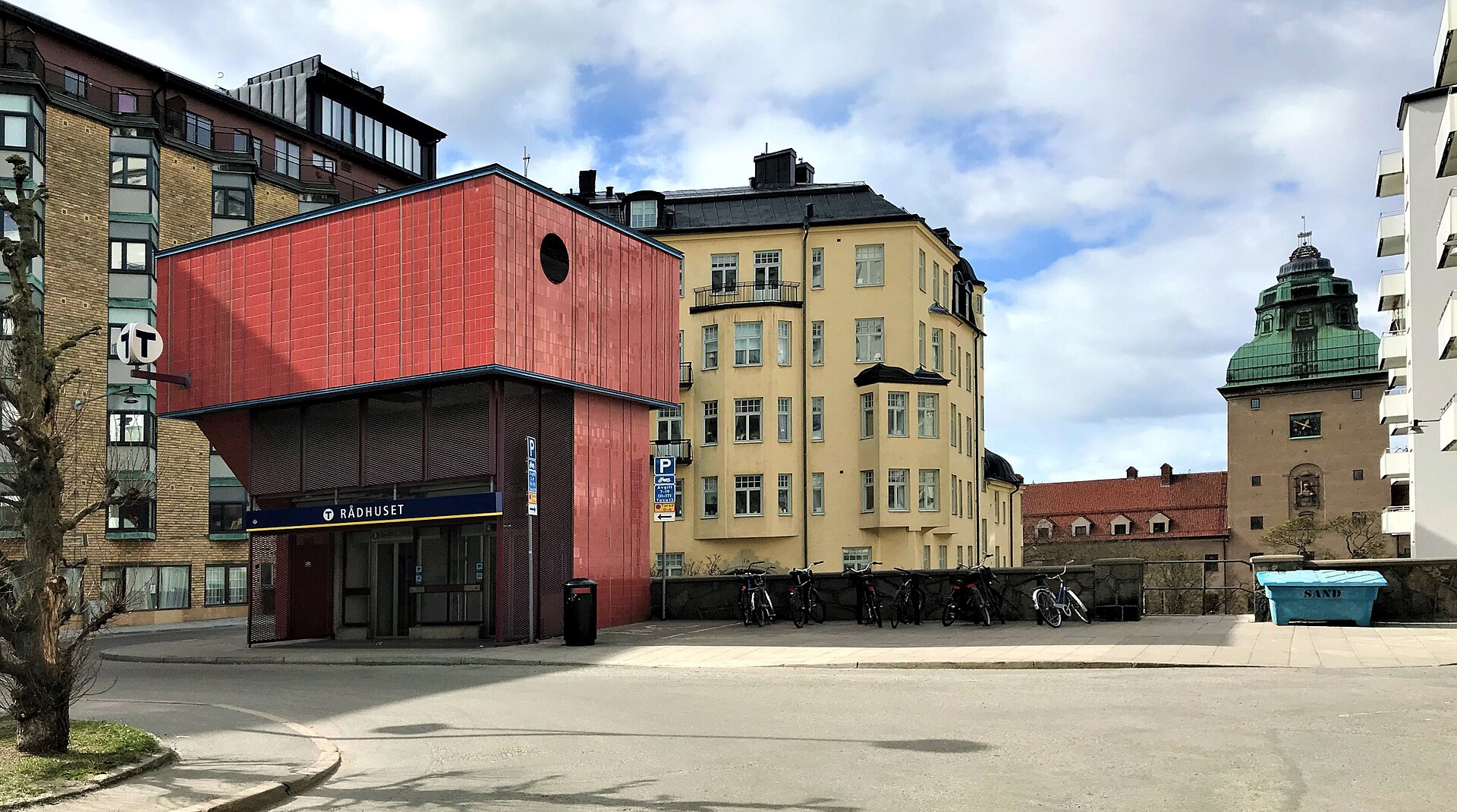 A red-tiled lift building with a blue Rådhuset metro sign at street level on Kungsklippan, with yellow apartment blocks behind