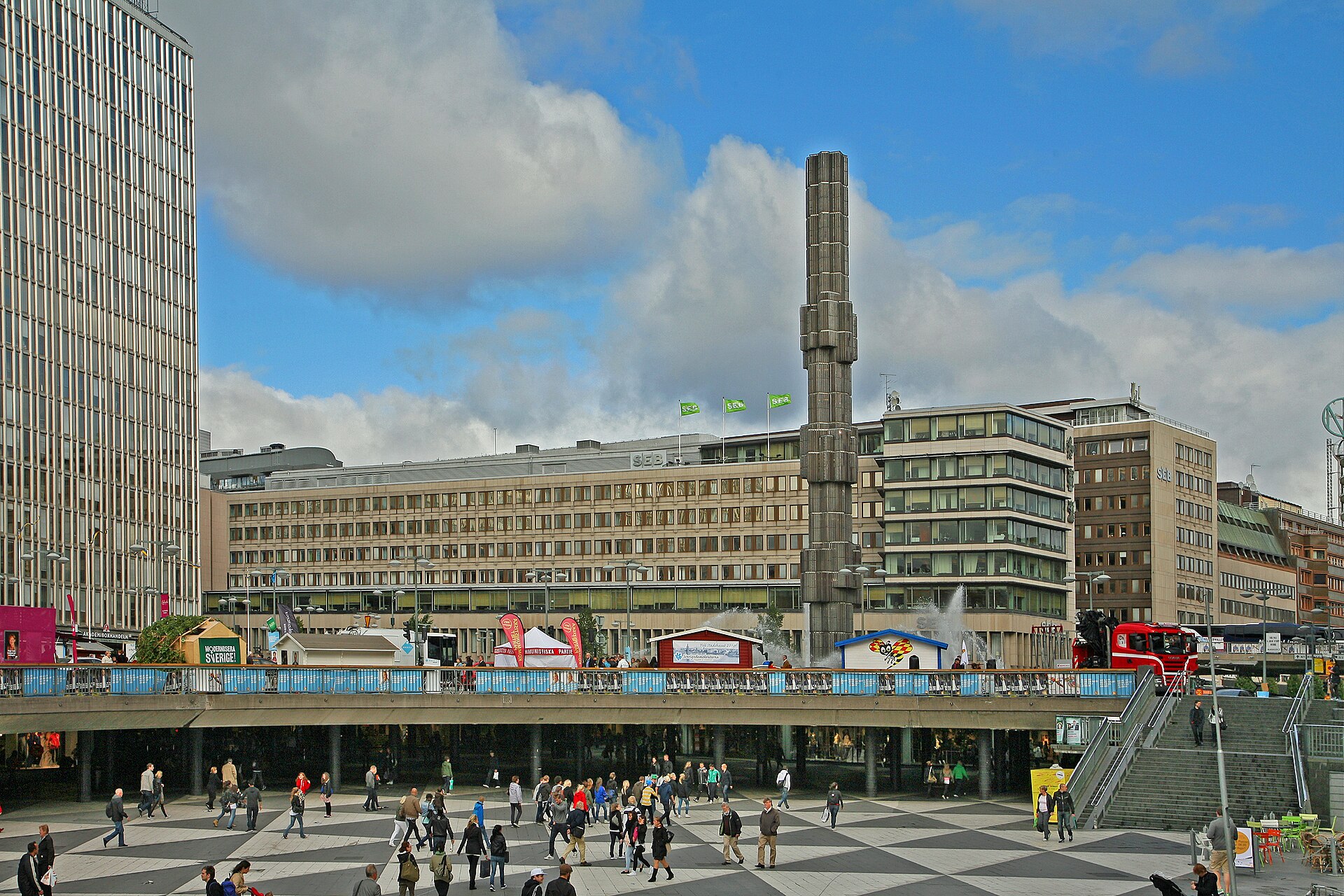 Sergels torg's black-and-white chequered plaza below street level, with the glass obelisk and office buildings behind and crowds crossing the square