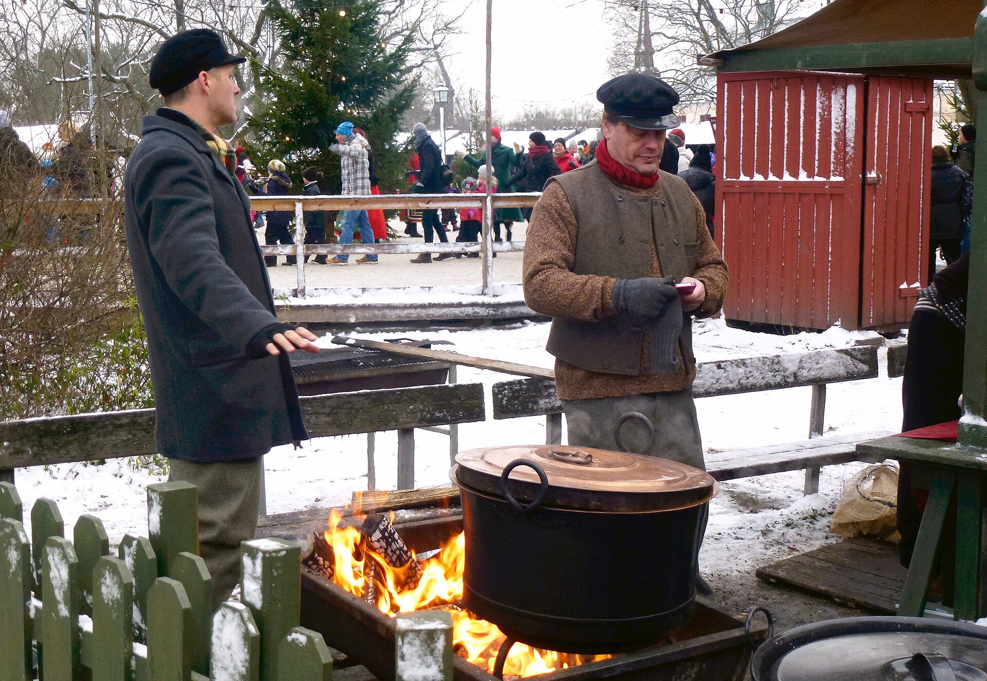 Costumed staff tending an open fire with a copper cauldron at Skansen's Christmas market in the snow