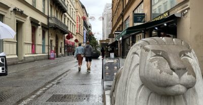 Shoppers on the pedestrianised Drottninggatan in Stockholm on a wet day, beside one of the concrete lion barriers