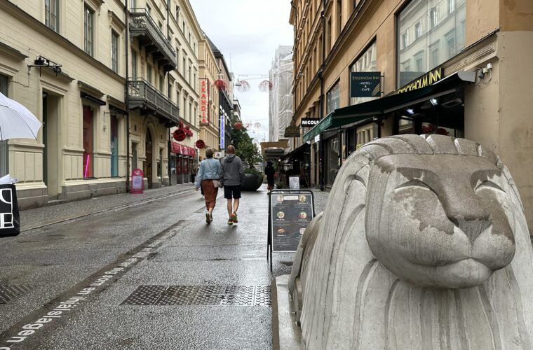 Shoppers on the pedestrianised Drottninggatan in Stockholm on a wet day, beside one of the concrete lion barriers