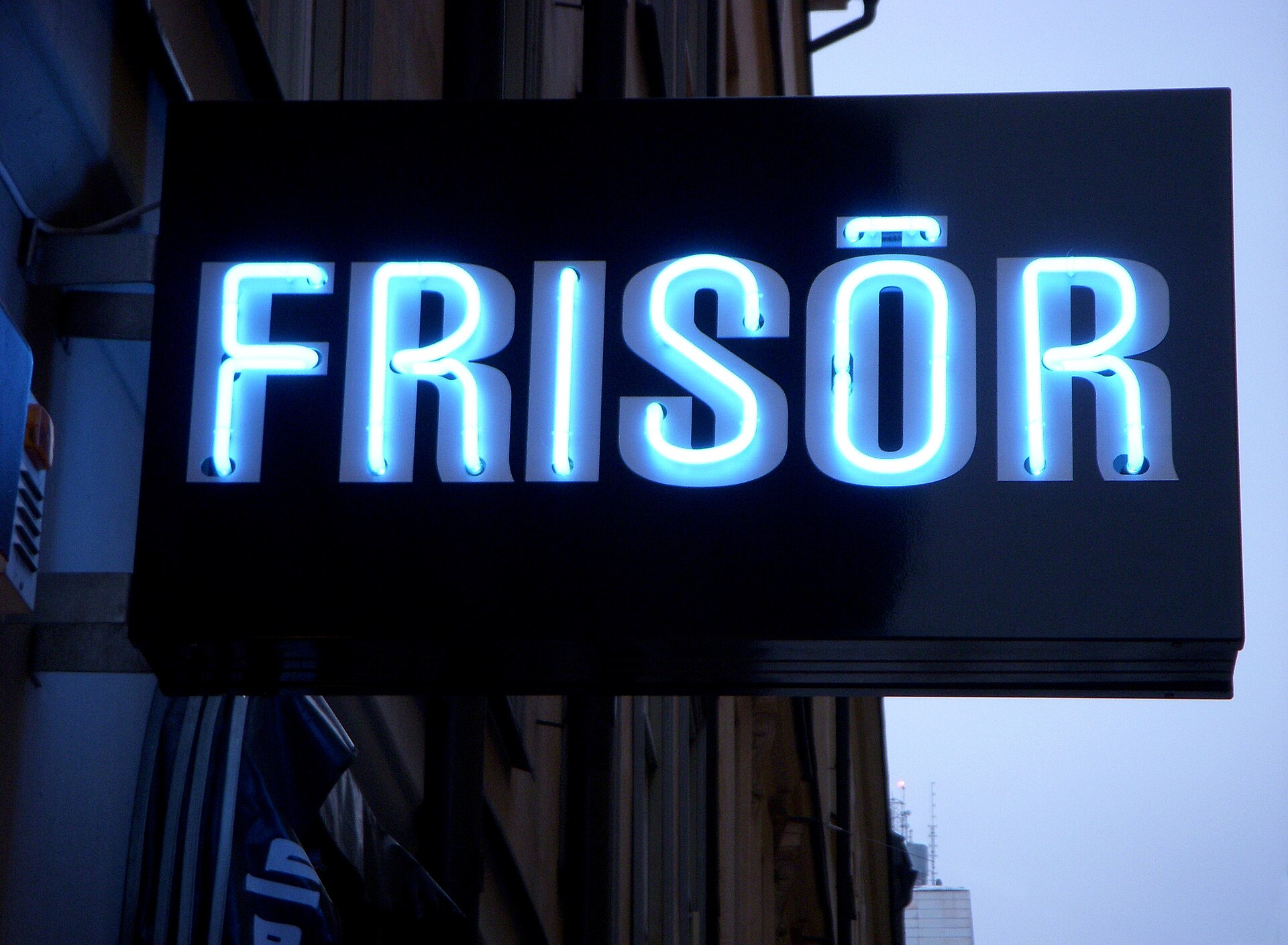 An illuminated blue neon sign reading FRISÖR outside a Stockholm hairdresser