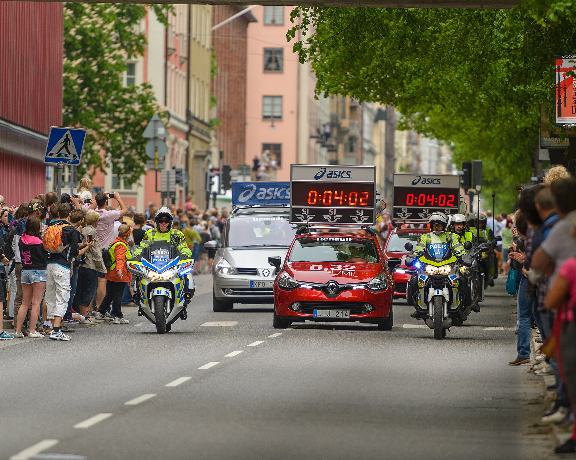 Police motorcycles and cars with digital race clocks lead the Stockholm Marathon along a tree-lined street as spectators line both pavements