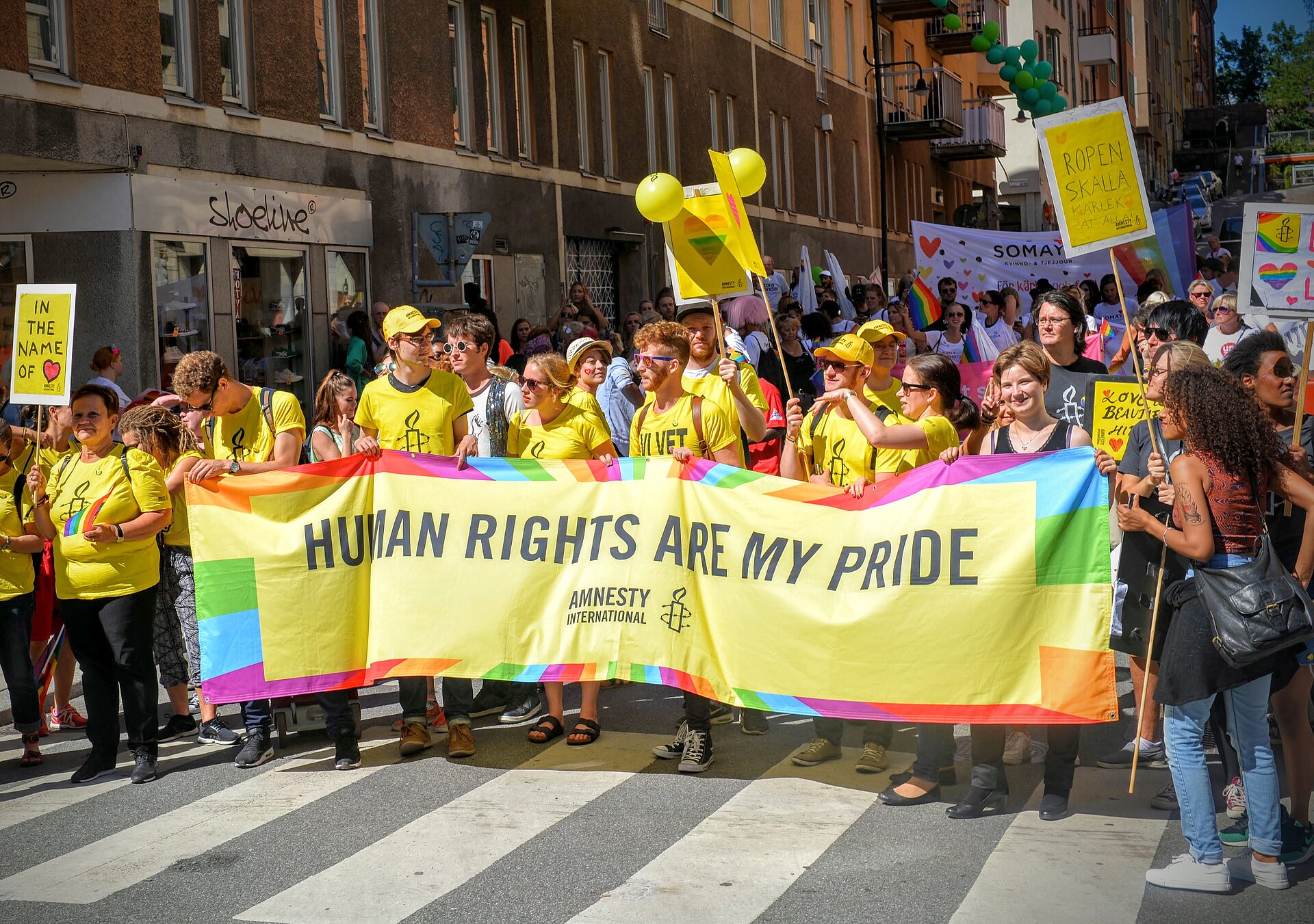 Marchers in yellow T-shirts carrying a rainbow-bordered banner reading Human Rights Are My Pride in the Stockholm Pride parade