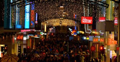 Dense evening crowds under Christmas lights on Drottninggatan in Stockholm, with illuminated shop signs
