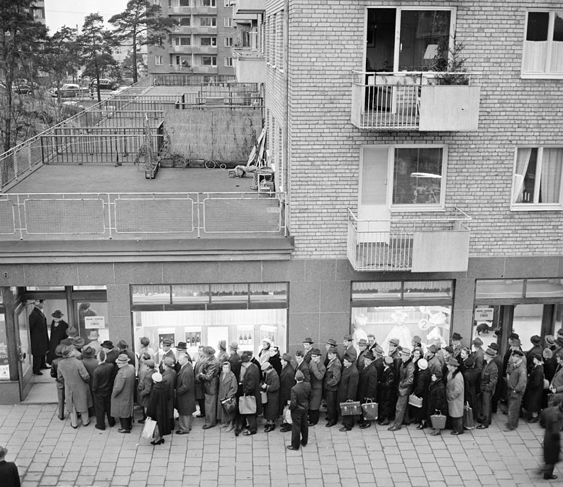 Black-and-white photograph of a long queue of men and women in winter coats and hats outside a Systembolaget shop on 23 December 1957