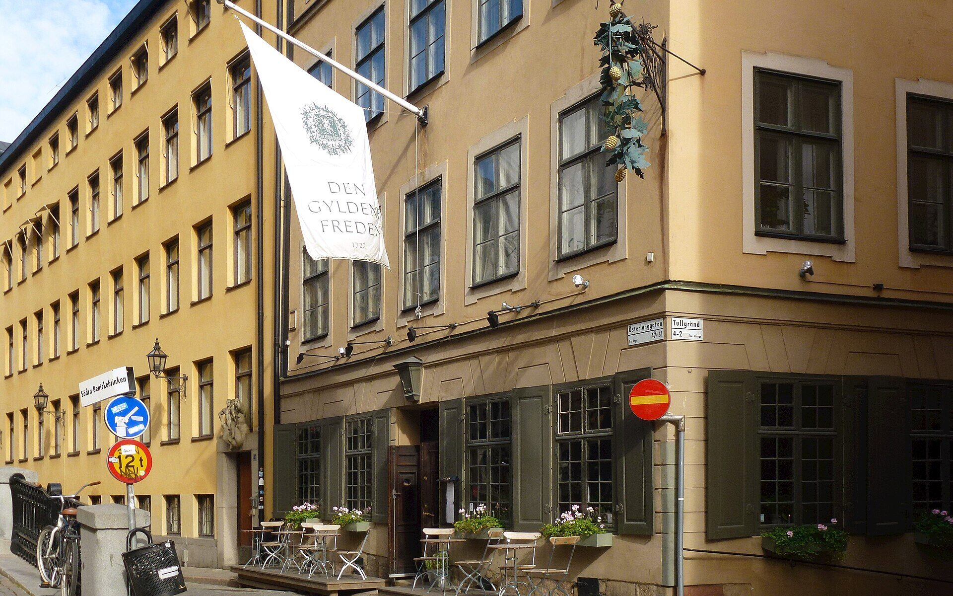 The ochre corner building of Den Gyldene Freden restaurant in Gamla Stan with its white banner and a small outdoor terrace
