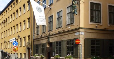 The ochre corner building of Den Gyldene Freden restaurant in Gamla Stan with its white banner and a small outdoor terrace