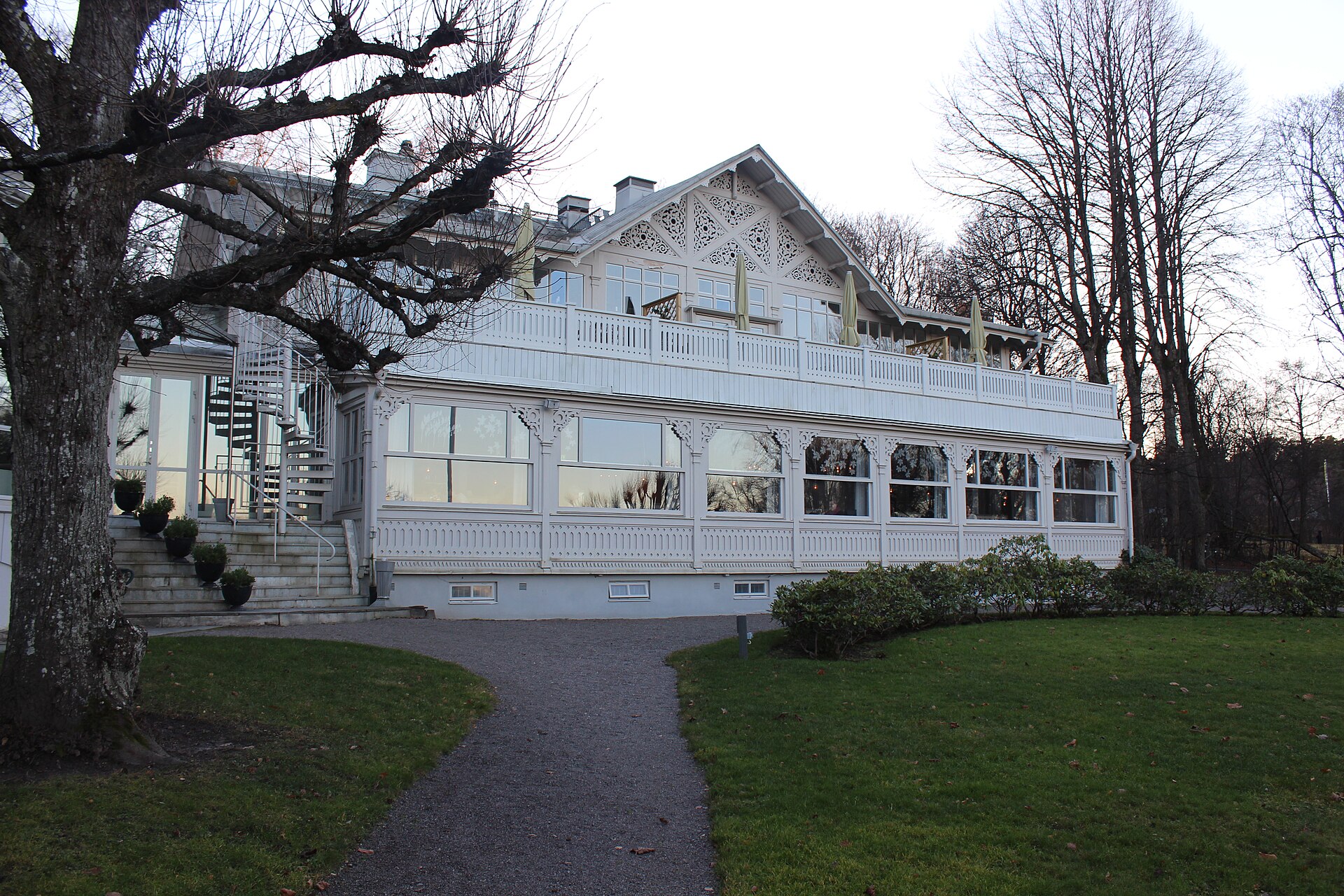 Ulriksdals Wärdshus, a white wooden inn with a carved gable and a long glassed-in veranda, among bare trees on a grey day